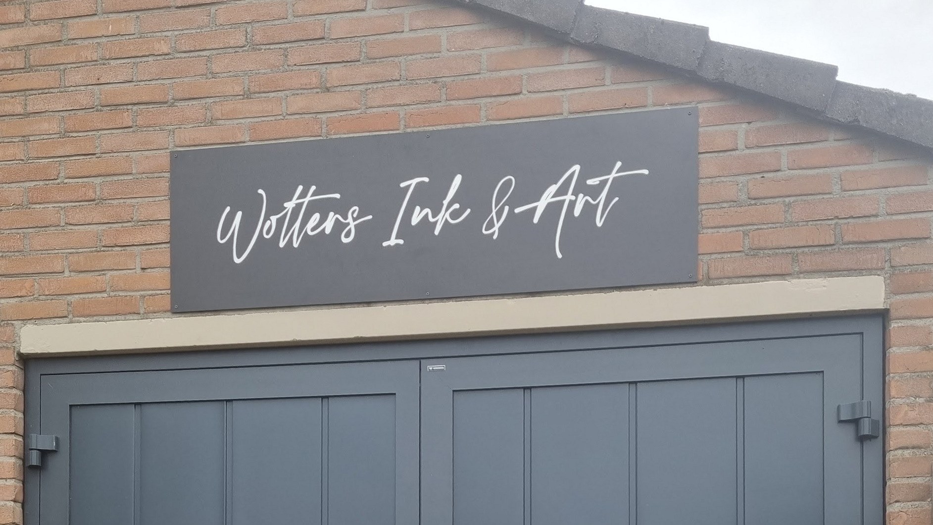 Het bord met Wolters Ink & Art in witte schrijfletters boven de deur van de studio
