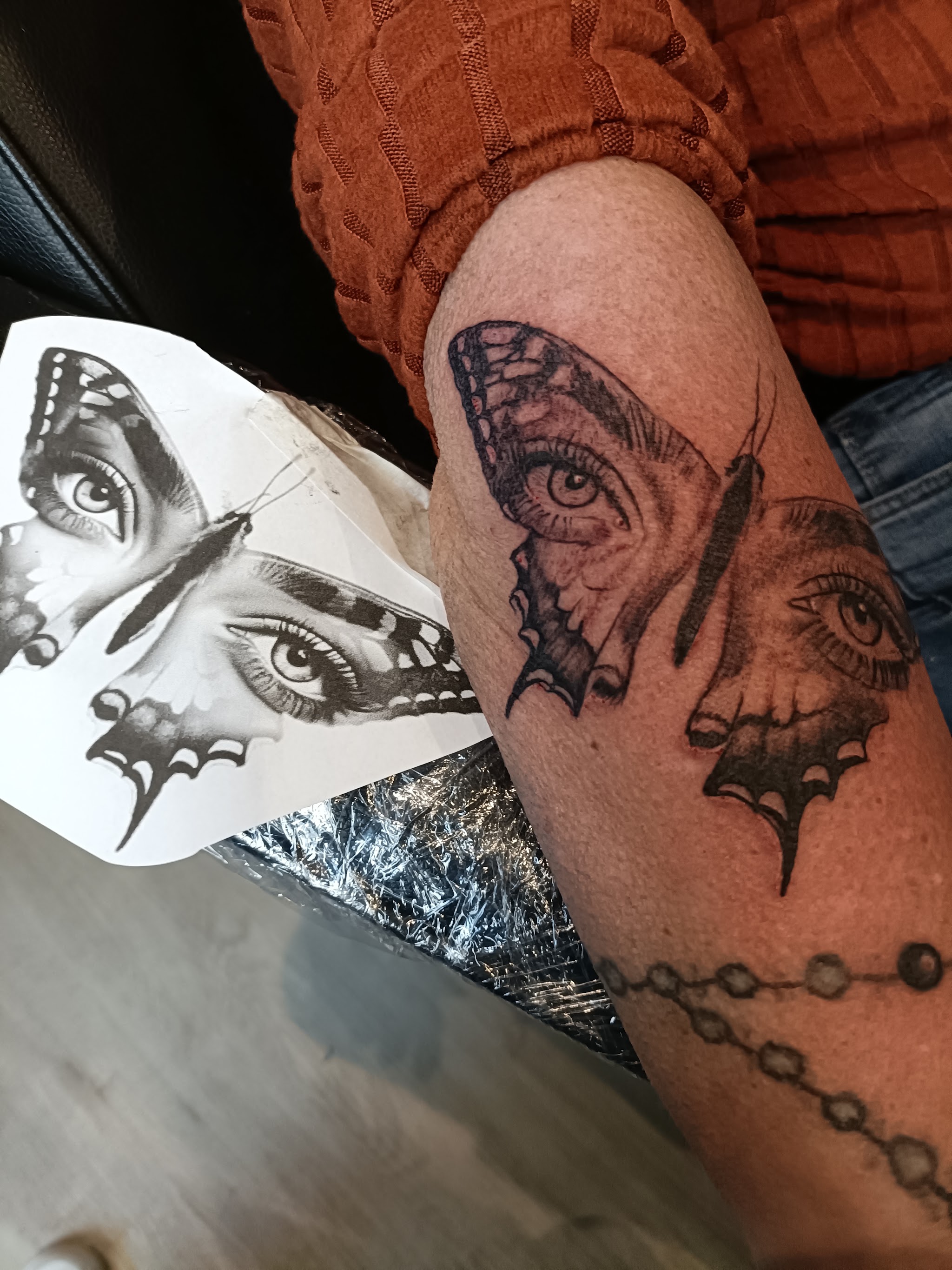 Ontwerp van een vlinder met ogen op papier, naast dezelfde tattoo op een onderarm