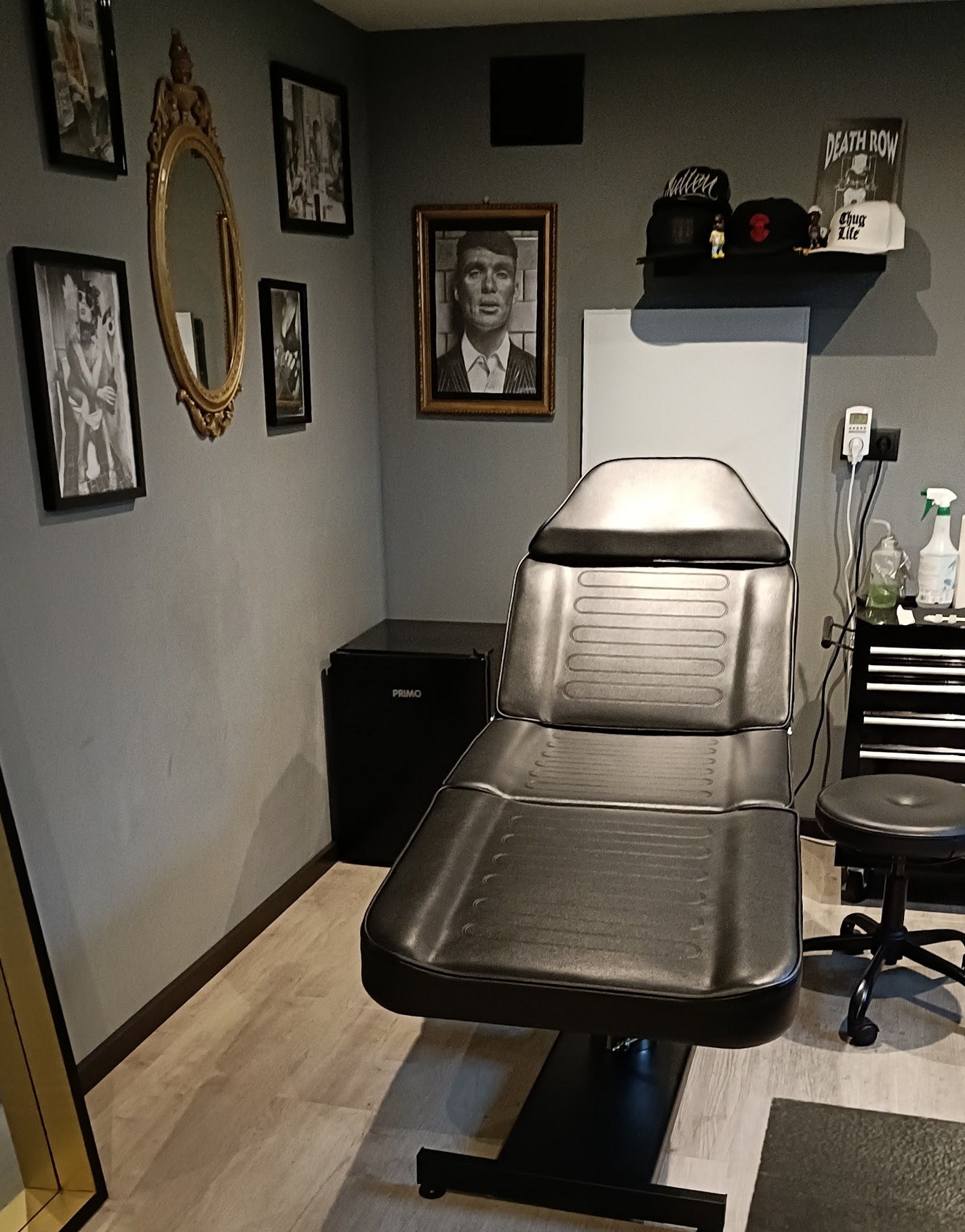 De studio: een zwarte tattoostoel, een werkplek en ingelijst werk aan de grijze wand